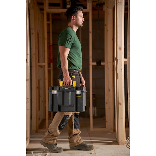 Stanley FMST1-71971 tool box with yellow handle carried by worker at construction site.