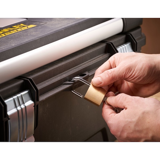 Close-up of hands unlocking a brass padlock attached to a black STANLEY toolbox.