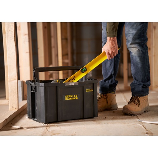 Stanley FMST1-75794 toolbox with handle, shown on construction site, person placing yellow level inside