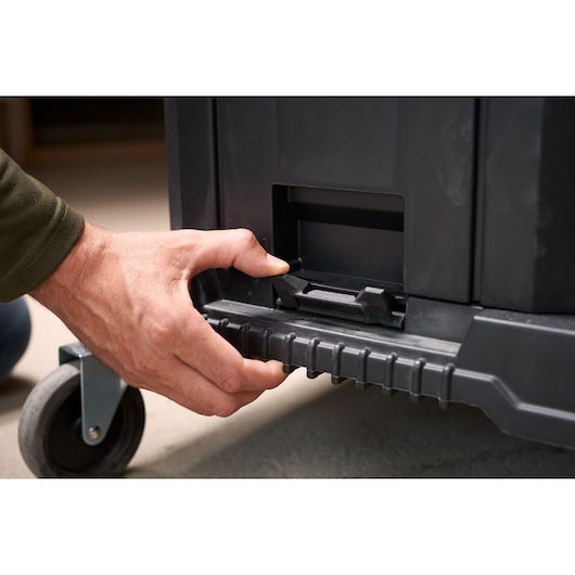 Photo of a hand operating the latch on a black STANLEY FMST1-80107 rolling toolbox, close-up view.