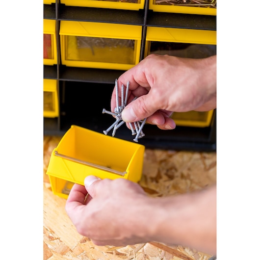 Photo of STANLEY FMST81077-1 yellow storage bin in use, holding nails, with hand placing nails inside.