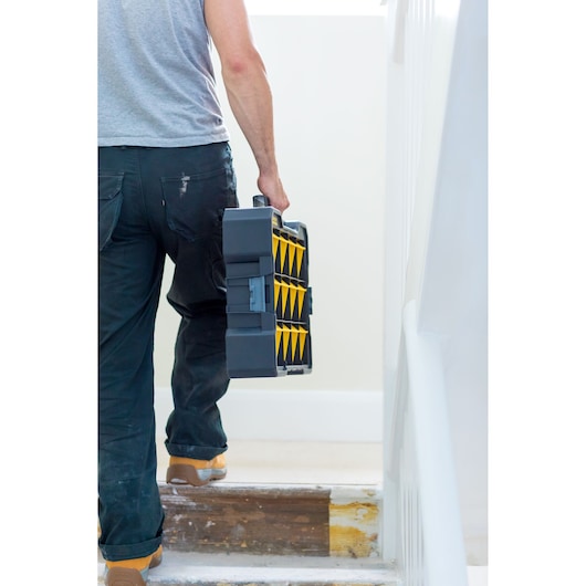 Photo of a person carrying a STANLEY FMST81077-1 tool organizer with yellow compartments up stairs.