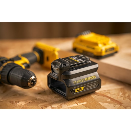 STANLEY SFMCB100 V20 lithium-ion battery, close-up on wooden workbench, drill and charger in background.