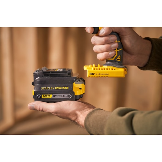 Photo of STANLEY FATMAX V20 lithium ion battery, SKU SFMCB100, held in hand, with 18V lithium tool connector nearby.
