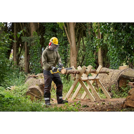 Photo of person using STANLEY SFMCCS730B chainsaw to cut wood on a sawhorse outdoors.