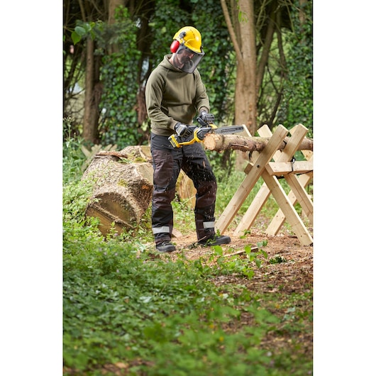 STANLEY SFMCCS730B chainsaw in use cutting wood outdoors, operator wearing safety gear, forestry setting.