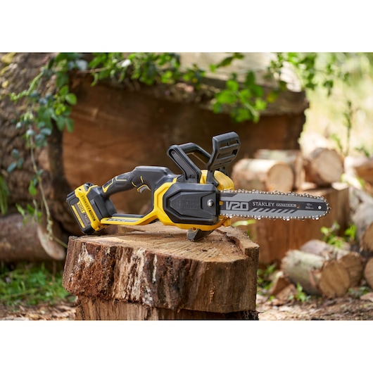STANLEY SFMCCS730B cordless chainsaw with yellow and black body, resting on a cut tree stump outdoors.
