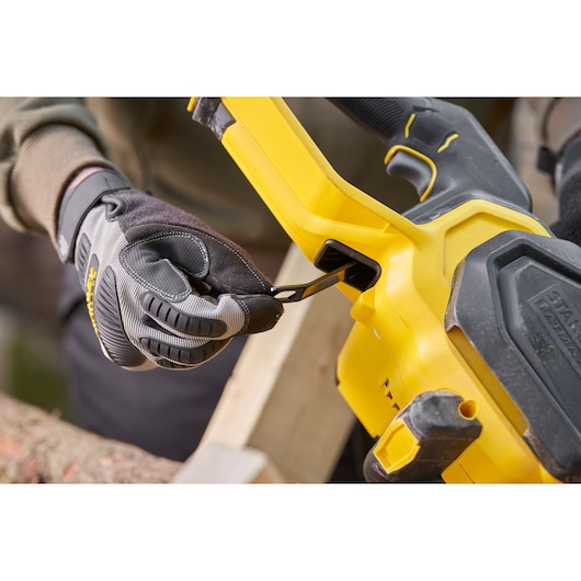 STANLEY SFMCCS730B chainsaw close-up, showing gloved hand engaging chain tension lever.