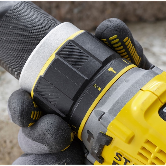 Close-up photo of STANLEY SFMCD721D2K drill with textured grip and adjustment ring held by gloved hand.