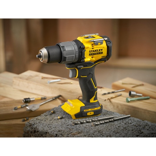 STANLEY SFMCD726B cordless drill in yellow and black, side angle, shown with drill bits on wood and concrete.