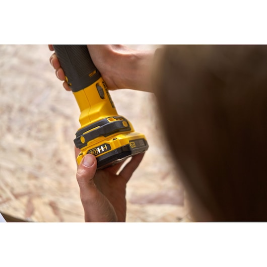 Close-up of hands holding STANLEY SFMCE500D2K cordless power tool on wooden surface.