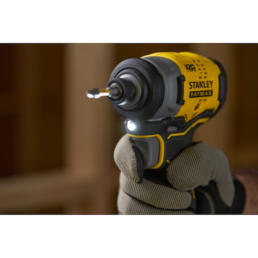 STANLEY SFMCF810B impact driver close-up in use, yellow and black, with LED light on, held by gloved hand.
