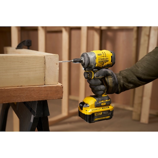 STANLEY SFMCF910B cordless impact driver being used to drive a screw into wood, side view, workshop setting.