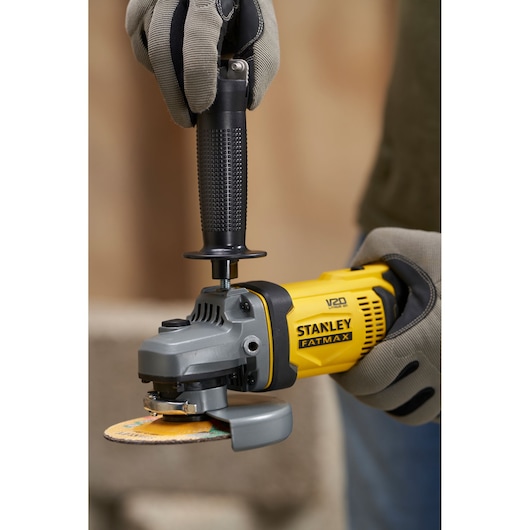 Photo of STANLEY SFMCG400B angle grinder held by gloved hands, yellow and black, close up.