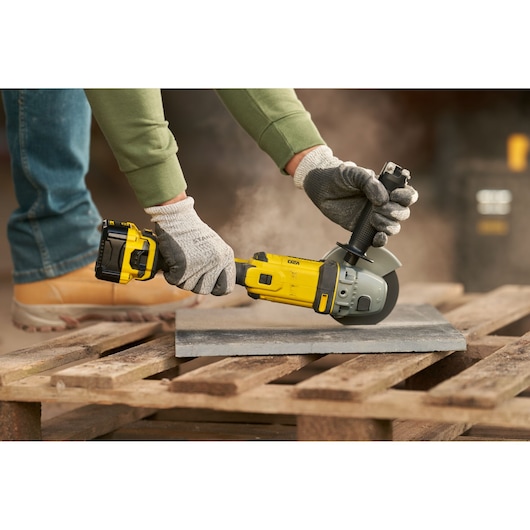 STANLEY SFMCG400M2K cordless angle grinder, yellow and black, in use on a slab outdoors.