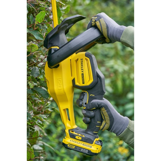 STANLEY SFMCHT650D1 cordless hedge trimmer in use, yellow and black body, trimming green hedge.