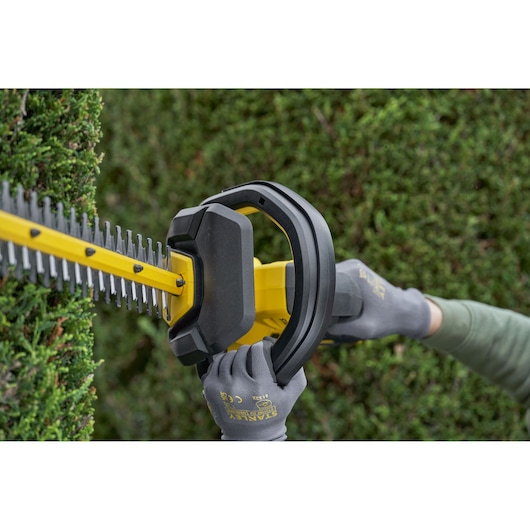 STANLEY SFMCHT655M1 hedge trimmer in use, close-up angle, cutting green bushes outdoors.