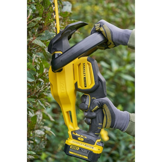 Photo of STANLEY SFMCHT655M1 hedge trimmer with yellow and black design in use trimming green bushes.
