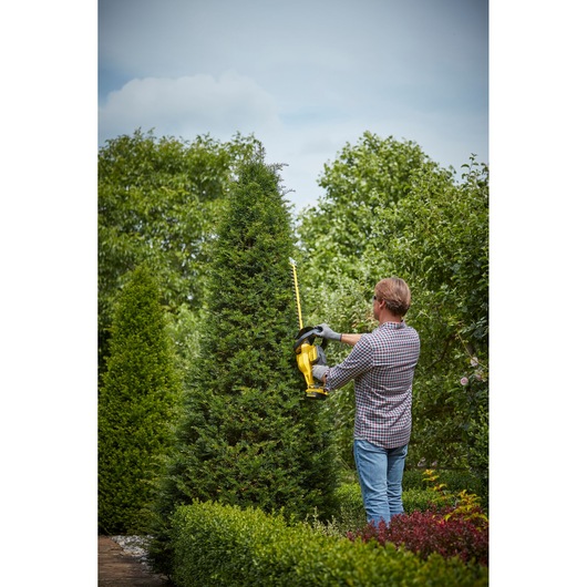 STANLEY SFMCHT855B hedge trimmer being used outdoors by a person trimming a tall green bush.