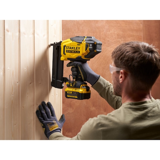 STANLEY SFMCN618B-XJ battery nailer tool used on wooden panel, side angle, yellow and black color.