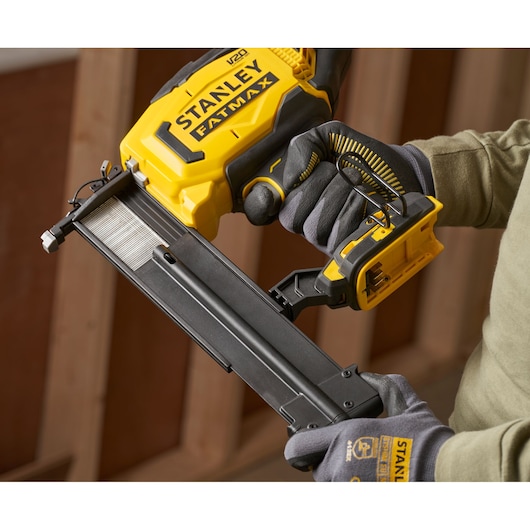 Photo of STANLEY SFMCN618B-XJ cordless nailer in use, yellow and black, shown held by gloved hands.