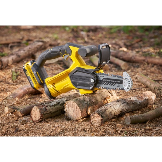 STANLEY SFMCPS415B cordless chainsaw, yellow and black, photographed cutting logs outdoors.
