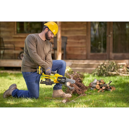 Photo of STANLEY SFMCPS515M1 cordless chainsaw in use, man cutting wood in a garden setting.