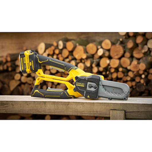 STANLEY SFMCPS515M1 cordless chainsaw, yellow and black, resting on wood table, log pile background.