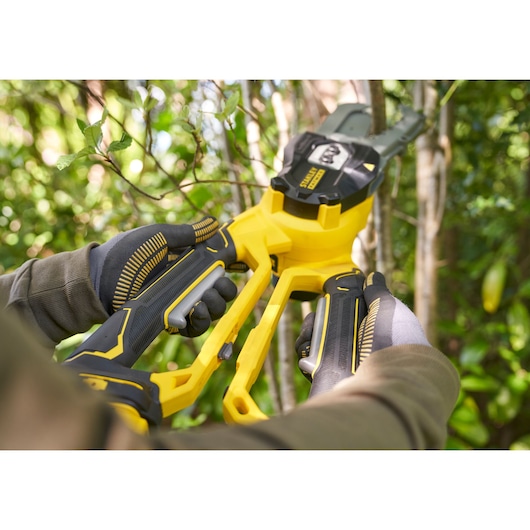 STANLEY SFMCPS515M1 cordless pruner in use outdoors, close-up showing yellow and black tool cutting branches.