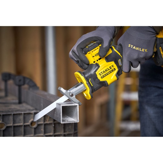 Photo of STANLEY SFMCS305B reciprocating saw cutting metal tube, close-up with gloved hands, tool in use.
