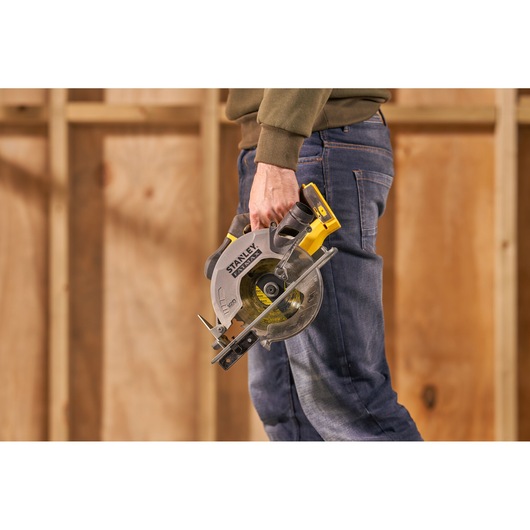 Stanley SFMCS500B cordless circular saw held by person, shown in a workshop setting.
