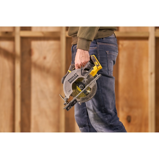 STANLEY SFMCS500M2K circular saw held by person in jeans, shown in a workshop setting.