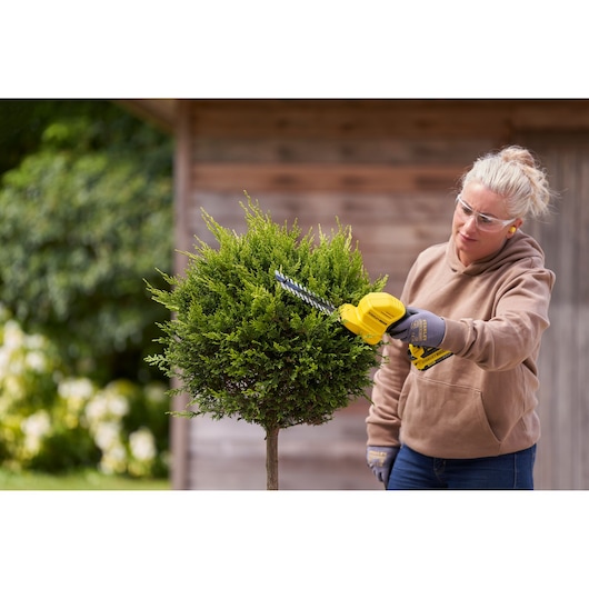 STANLEY STCSS20B hedge trimmer in use trimming a small green bush in a garden.