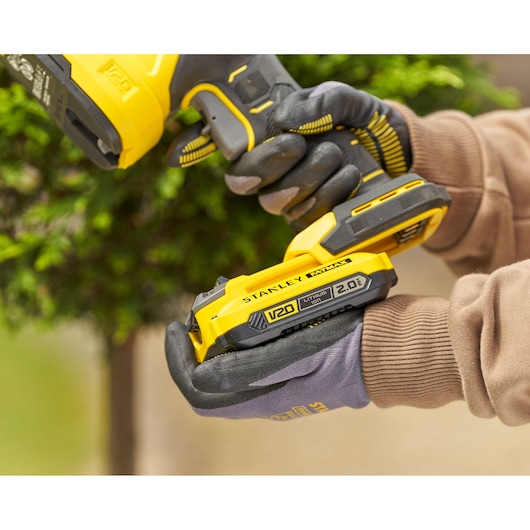 Stanley STCSS20B yellow V20 lithium ion battery held in gloved hands, close-up outdoor view.