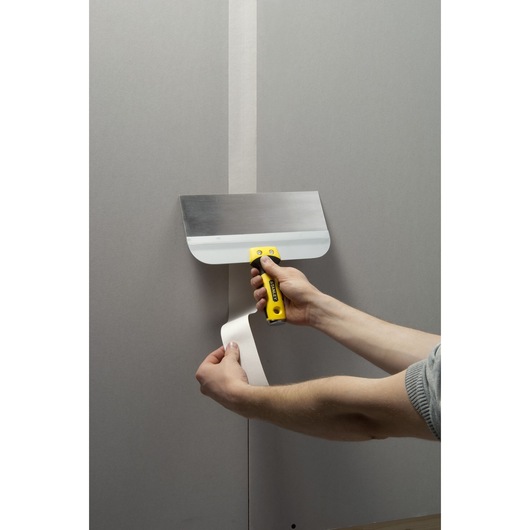 Photo of STANLEY STHT0-05771 drywall taping knife with yellow handle applying joint tape to plasterboard wall.