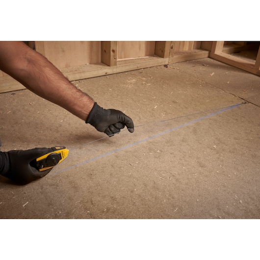 Photo of STANLEY STHT0-47147 chalk line tool in use, marking a straight blue line on a wooden floor.