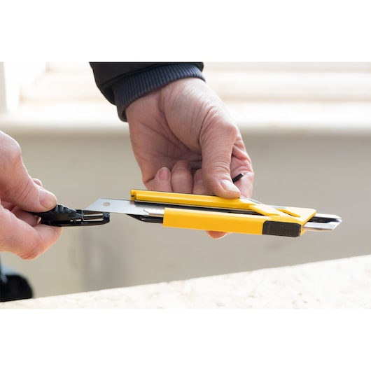 STANLEY STHT10266-1 yellow utility knife held in hand, close-up angle, safety blade extended.