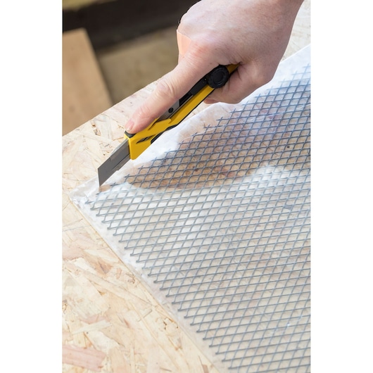 STANLEY STHT10268-1 utility knife cutting mesh material on wooden surface, close-up angle.
