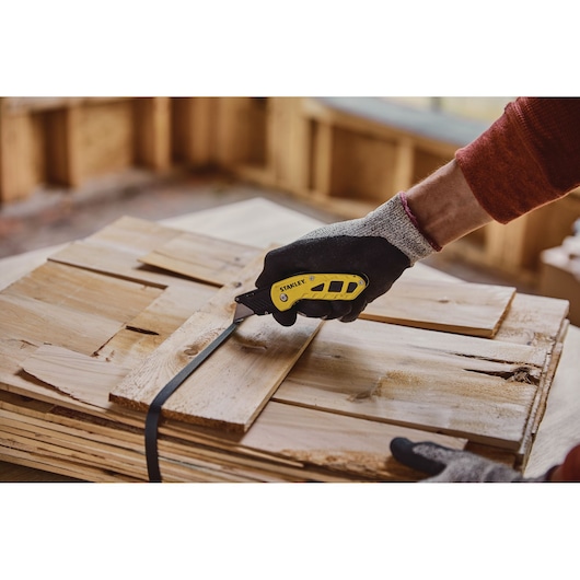 STANLEY STHT10424-0 folding utility knife cutting black strap on stacked wood, close-up view.