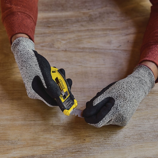 Photo of STANLEY STHT10432-0 utility knife held in gloved hands, blade extended, on wooden surface.