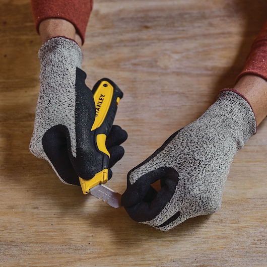 Stanley STHT10479-0 utility knife held with gloves, blade being changed, tabletop view, photography.
