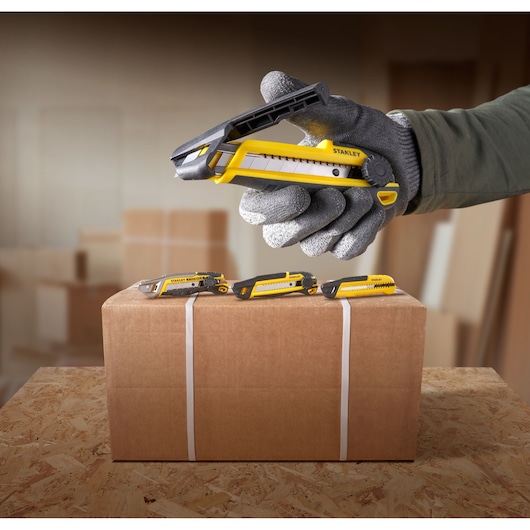STANLEY STHT10500-0 yellow and black utility knife in use, opening cardboard box, seen from side angle.