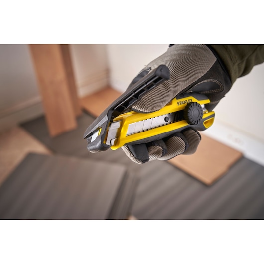 Photo of STANLEY STHT10500-0 utility knife with segmented blade, yellow and black, held in gloved hand.