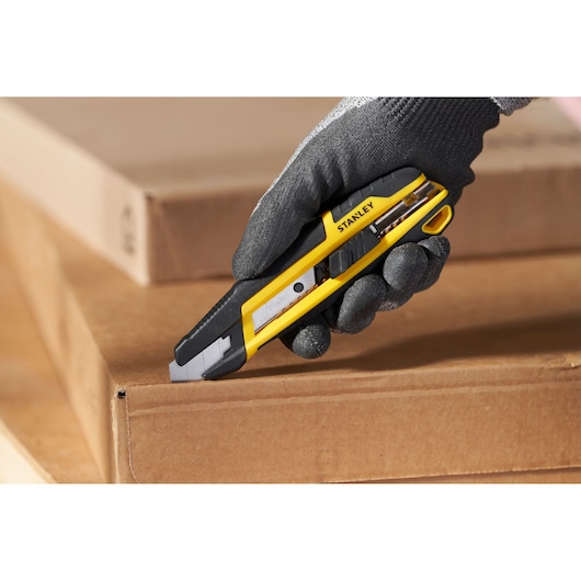 STANLEY STHT10501-0 utility knife cutting cardboard, close-up in gloved hand, tool photography.