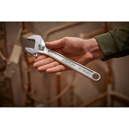 Photo of a STANLEY STHT13121-0 adjustable wrench held in a hand, silver color, used in a workshop setting.