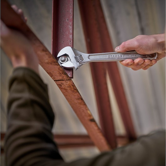 Stanley STHT13122-0 adjustable wrench in use tightening bolt on red metal beam, close-up photography.