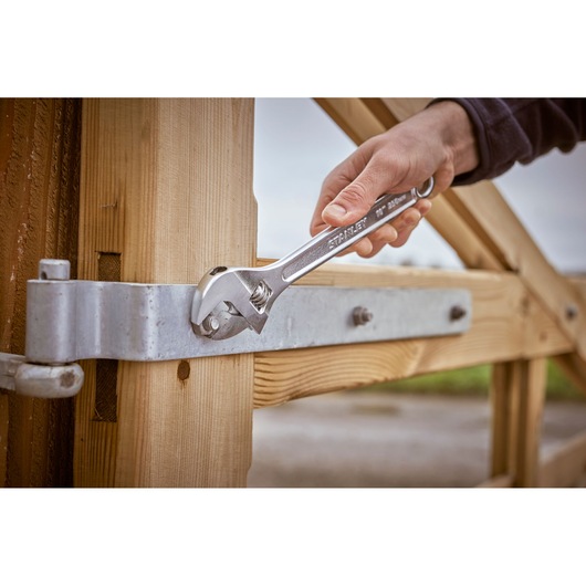 Photo of STANLEY STHT13123-0 adjustable wrench tightening a bolt on a metal hinge attached to a wooden gate.