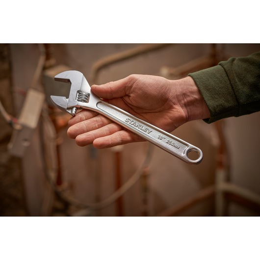 Photo of STANLEY STHT13123-0 adjustable wrench, 250mm size, held in hand against a background of pipes.