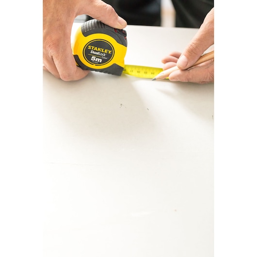Photo of STANLEY STHT36803-0 tape measure, yellow and black, being used to measure and mark on a white surface.