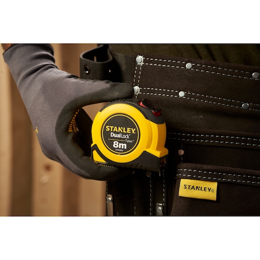 Photo of STANLEY STHT36804-0 DualLock 8m tape measure in tool belt, held by gloved hand.
